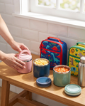 Pink, blue and green lunch jars packed with kids' lunches on a kitchen bench